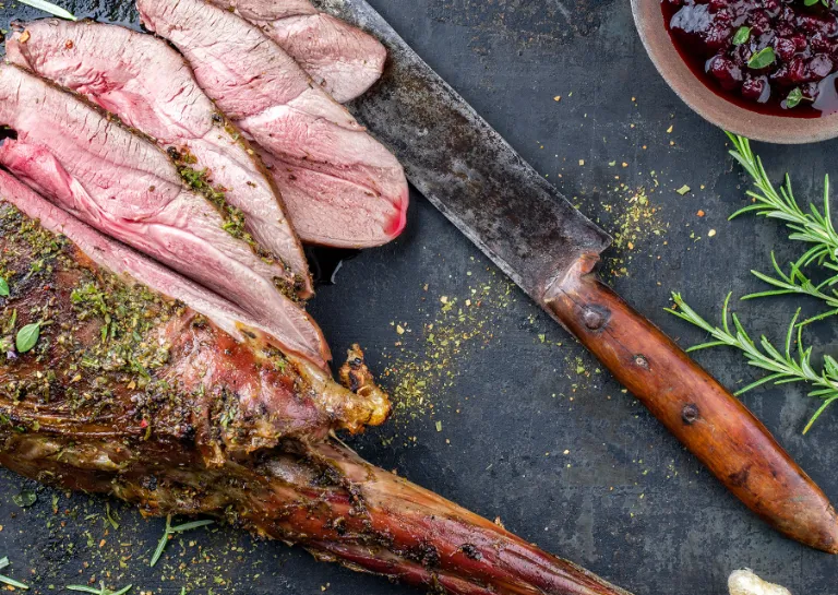 Gegrillte Rehkeule liegt in Scheiben geschnitten auf einer Schieferplatte