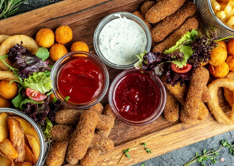 Verschiedene frittierte Speisen, wie Zwiebelringe, Pommes, Mozzarella-Sticks und Kroketten, auf einem Holzbrett angerichtet