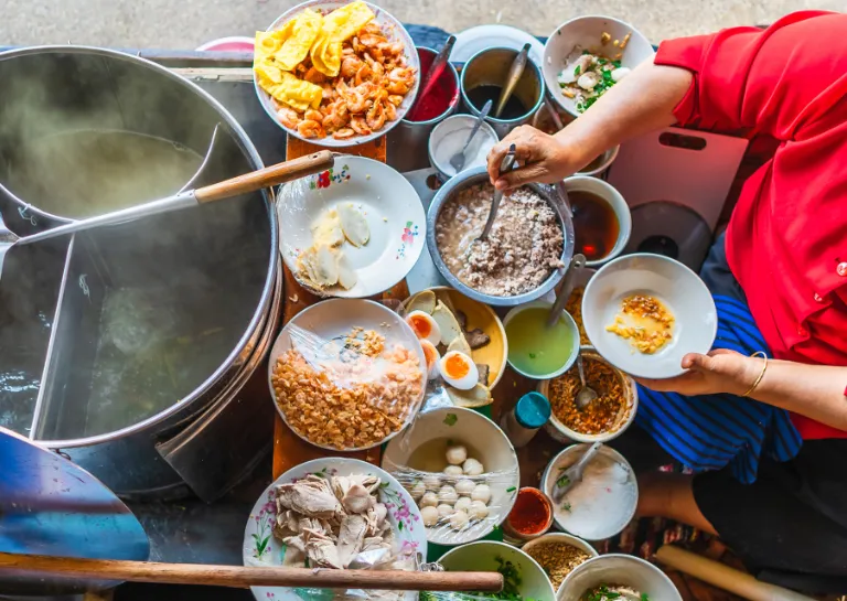 Frau in einer schwimmenden thailändischen Streetfood-Garküche bereitet ein typisch thailändische Gericht zu