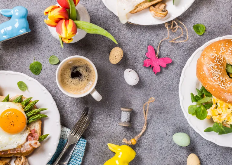 gedeckter Tisch für den Osterbrunch mit bunten Eiern, einem Teller mit Spiegelei und einem Teller mit einem Bagel.