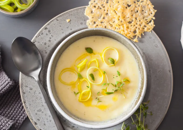 Käse-Lauch-Suppe in grauem Suppenteller mit Parmesan-Gitter an der Seite