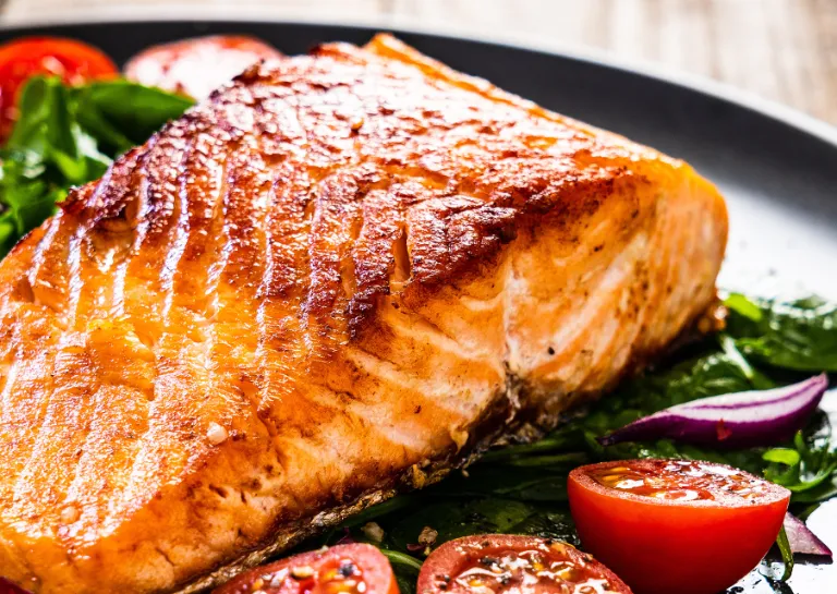 Ein gegrilltes Lachsfilet liegt auf einem Salatbett auf einem schwarzen Teller