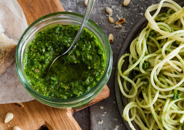 Mangold-Pesto im Glas neben einem Teller mit Spaghetti mit Mangold-Pesto