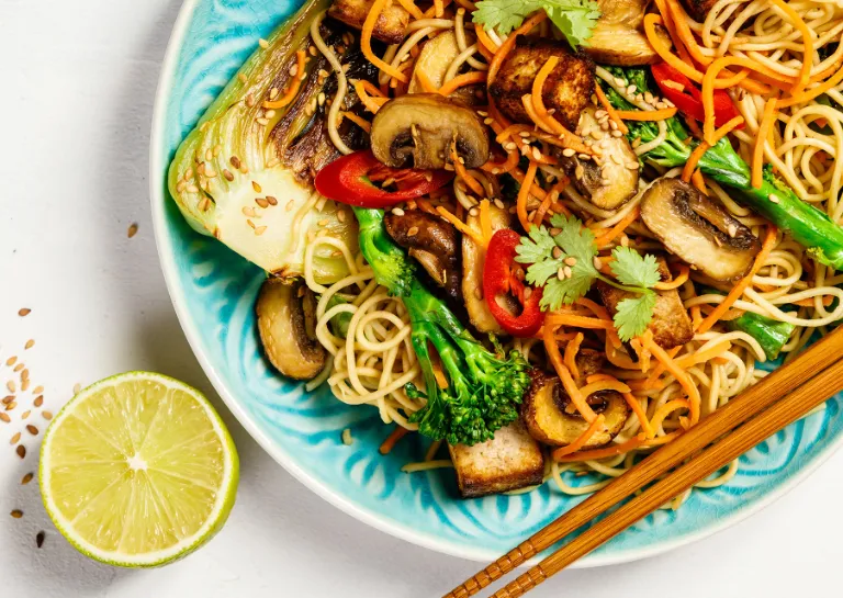 Pad Thai auf einem blauen Teller angerichtet und mit Stäbchen serviert