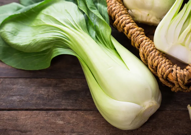 Mehrere Pak Choi in einem Korb, zusätzlich liegt ein ganzer und ein halber Pak Choi davor