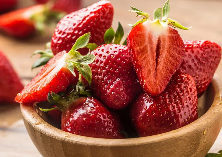Frische Erdbeeren in einer Holzschale und dahinter auf einem Holztisch verteilt.