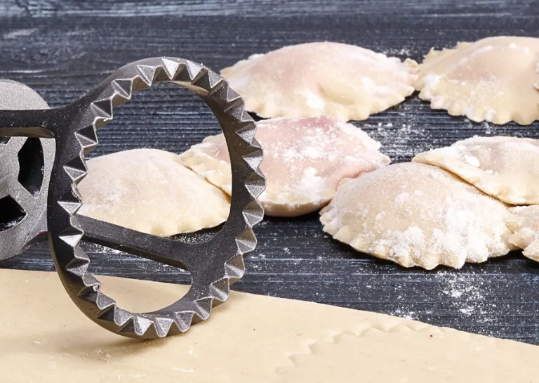 Teigtaschen fertig gefaltet mit rohem Nudelteig und einem Stechwerkzeug. 