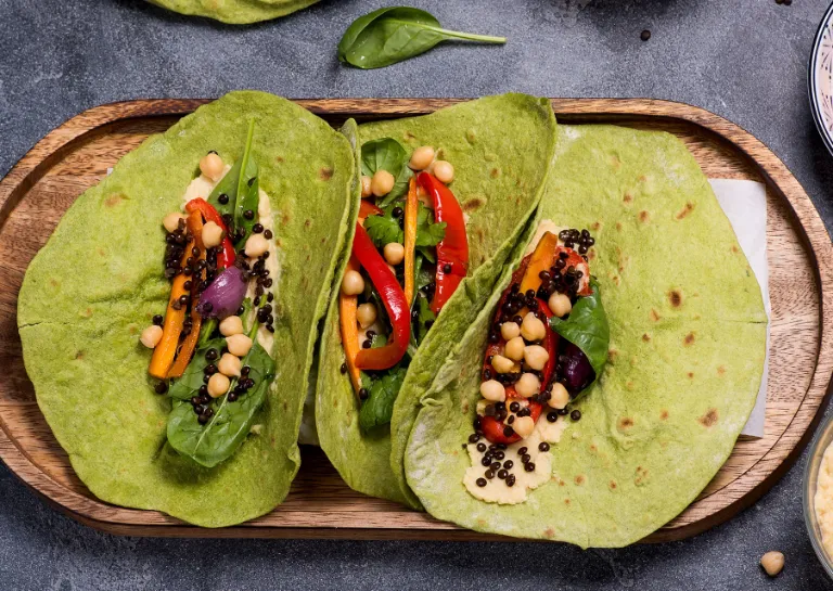 grüne Tortillafladen auf einem Holzbrett angerichtet mit Hummus und Grillgemüse