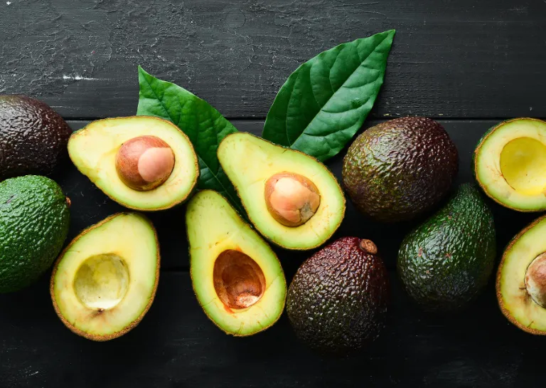 Mehrere Avocados nebeneinander auf einem dunklen Tisch