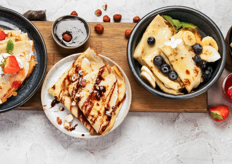 Crêpes gefüllt mit Nutella, Crêpes gefüllt mit Erdbeeren und Sahne, Crêpes belegt mit Blaubeeren und Banane und Crêpes belegt mit Orangenscheiben