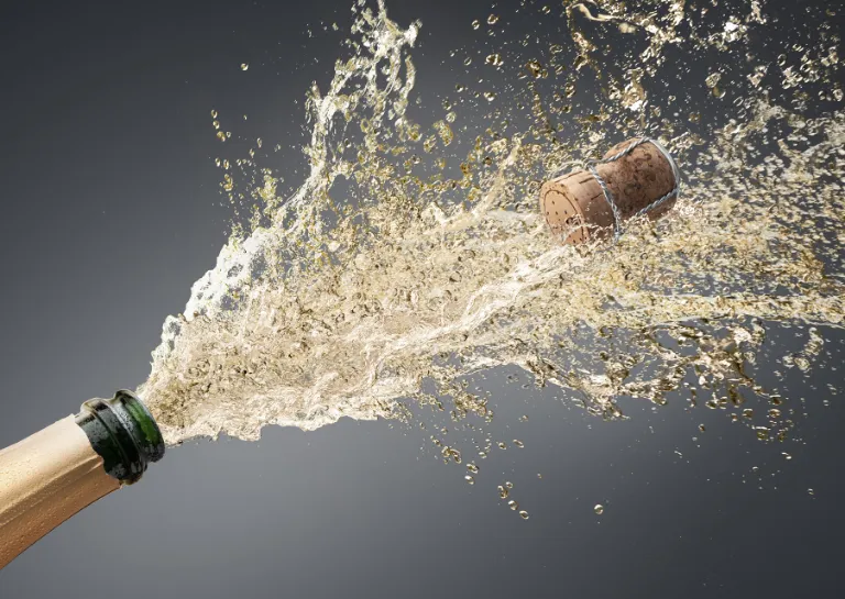 Geöffnete Champagnerflasche, Champagner spritzt heraus und der Korken fliegt weg