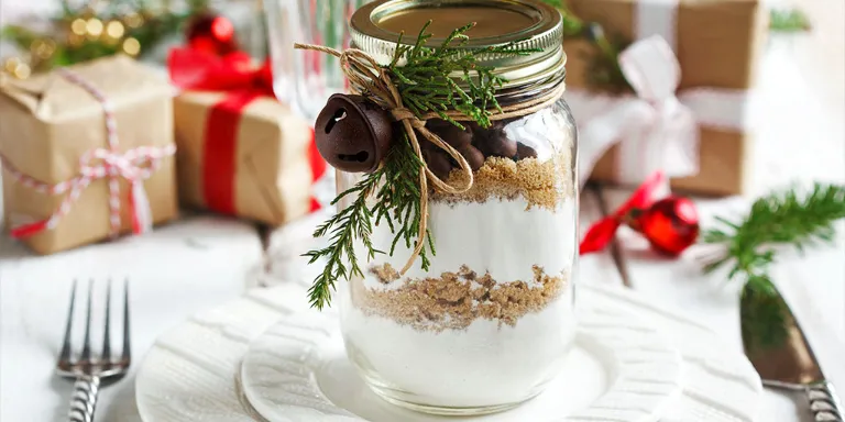 Geschenke aus der Küche Risottozutaten in einem Weckglas geschichtet mit einem Tannenzweig dekoriert und auf einem weißen teller stehend. Im Hintergrund sind kleine Geschenke platziert.