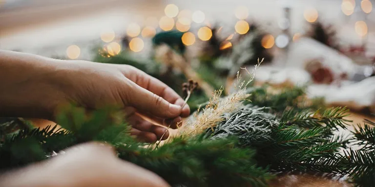 ein grüner Tannenzweig wird weihnachtlich mit Lichterketten und anderer Deko geschmückt