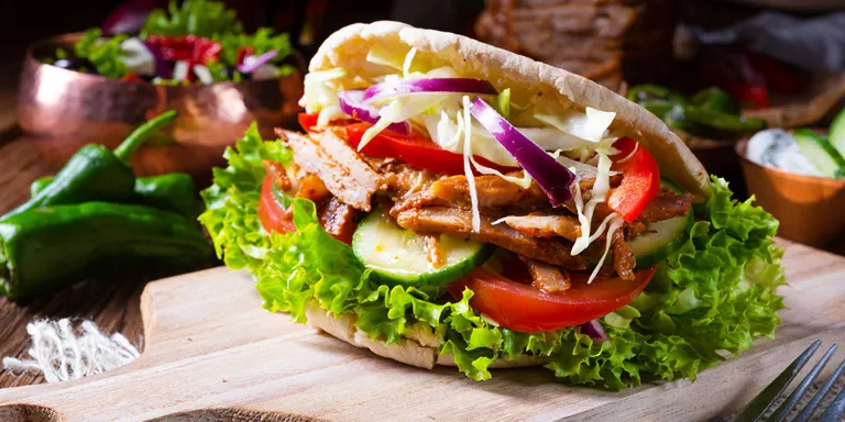 Döner Grillspieß vom Grill angerichtet in einer Pita mit Salat, Tomaten, Gurken, Paprika und Zwiebeln.