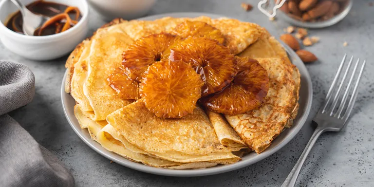 Crêpe Suzette mit Orangenscheiben dekoriert auf einem grauen Teller