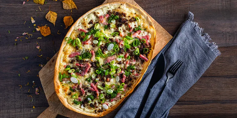 Wildschwein Flammkuchen und Zhug auf einem Holzbrett angerichtet