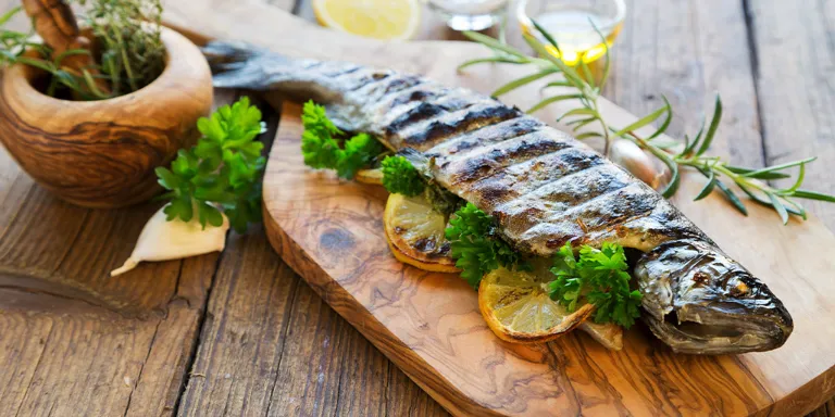 gegrillte Forelle auf Holzbrett mit Kräutern und Zitrone angerichtet auf einem Tisch 
