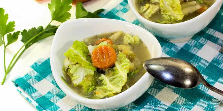 Wirsingsuppe mit Parmesan und Möhren angerichtet in einer kleinen Schale auf einer blau-weiß karierten Tischdecke