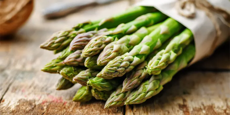 Stangen grüner Spargel liegen zusammengebunden auf einem Tisch
