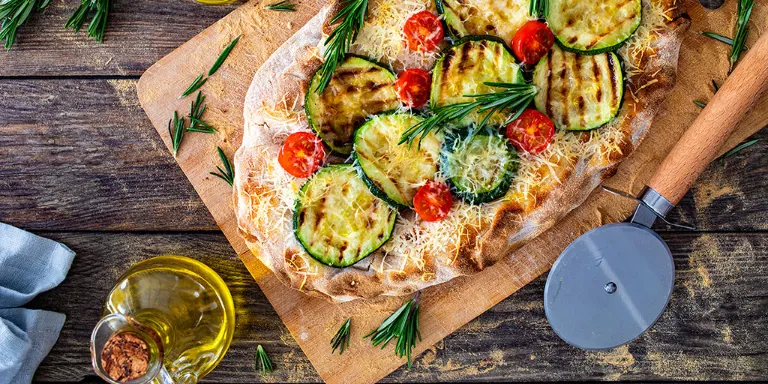 Frische Pinsa mit Zucchini vom Grill angerichtet auf einem Holzbrett.