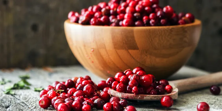 Preiselbeeren auf einem Holzlöffel und im Hintergrund in einer großen Holzschale