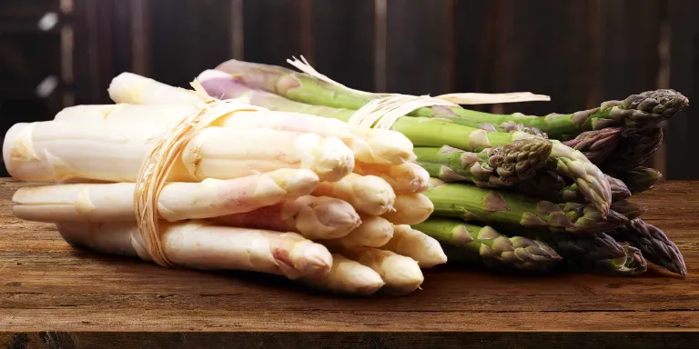 Ein Bund weißer und ein Bund grüner Spargel liegen nebeneinander auf einem Tisch.