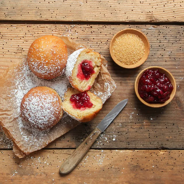 Berliner und Schüsselchen mit Marmelade und Zucker auf einem Holztisch
