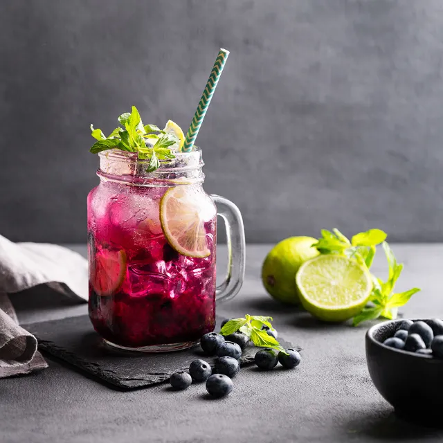 Alkoholfreier Cocktail mit Heidelbeeren und Limette in einem Glas mit Eiswürfeln und Strohhalm auf einem Tisch