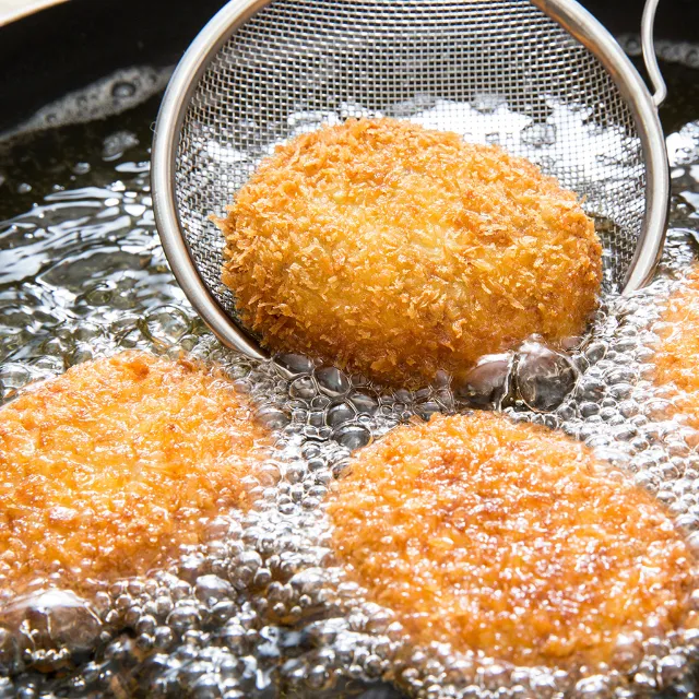 Drei Camemberts werden in heißem Fett ausgebacken, einer wird mit einer Schöpfkeller herausgenommen 