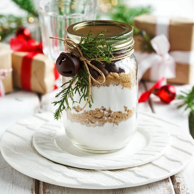 Geschenke aus der Küche Risottozutaten in einem Weckglas geschichtet mit einem Tannenzweig dekoriert und auf einem weißen teller stehend. Im Hintergrund sind kleine Geschenke platziert.