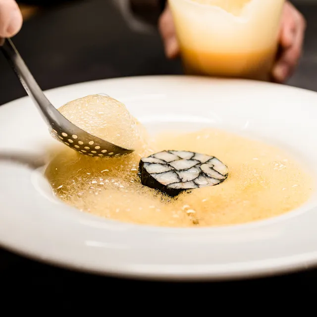 Molekularküche - Suppe als Schaum wird mit einer Kelle in einen Teller gefüllt. 