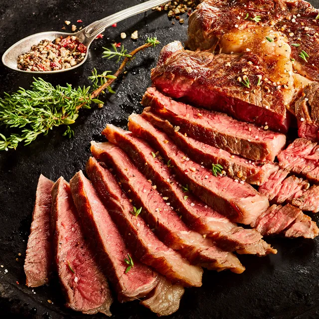 Steak mit Kaffee-Rub, aufgeschnitten auf einem schwarzen Untergrund, im Hintergrund ein Löffel mit Kaffee-Rub