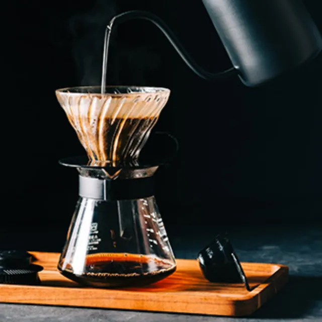 Ein Kaffeefilter aus Glas steht auf einer Kaffeekanne aus Glas, es wird gerade Wasser eingegossen, um Kaffee zu kochen