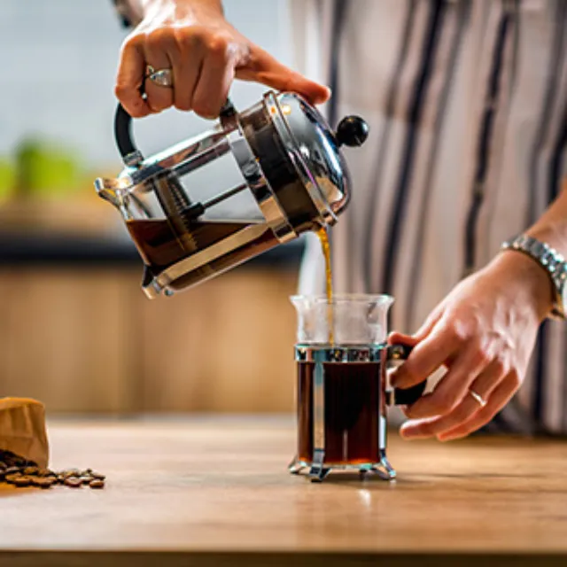 Kaffee, der mit einer French Press zubereitet wurde, wird in eine Tasse aus Glas ausgegossen