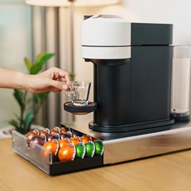 Kapselmaschine für Kaffee auf einem Tisch, darunter eine Schublade mit Kaffeekapseln