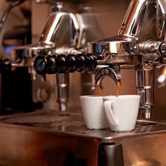 Zwei Espressotassen unter einer Siebträgermaschine, aus der Esprosse herausläuft