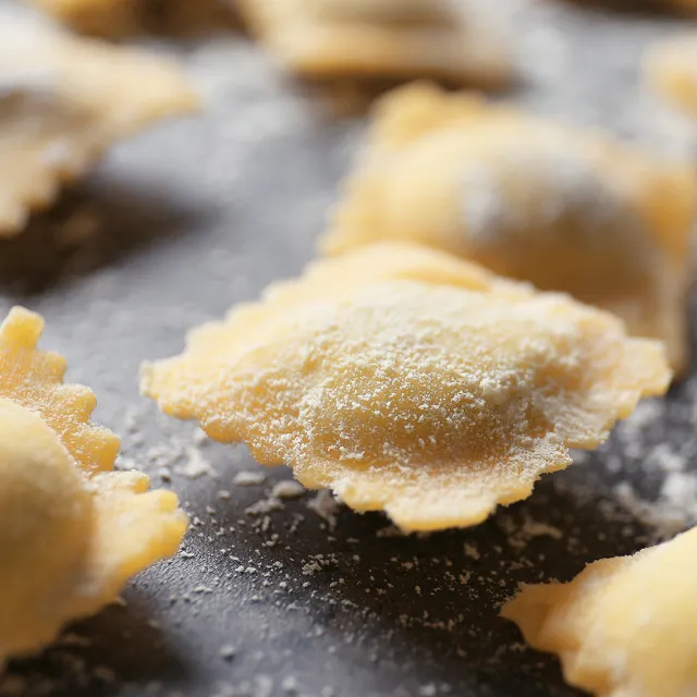 Selbstgemachte Pasta, die mit Birne gefüllt ist und noch roh auf einem Holzbrett liegt