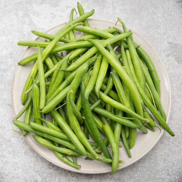Grüne Bohnen auf einem weißen Teller, der auf einer grauen Fläche steht