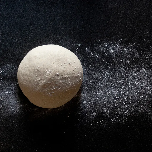 Eine Kugel Hefeteig auf einer schwarzen Tischoberfläche