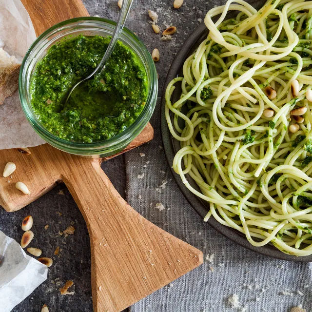 Mangold-Pesto im Glas neben einem Teller mit Spaghetti mit Mangold-Pesto