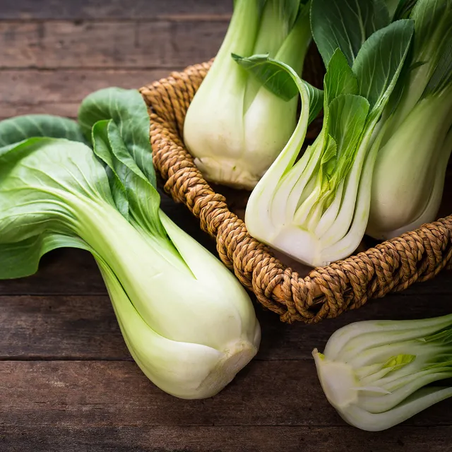 Zwei ganze und ein halber Pak Choi im Korb, zusätzlich liegt ein ganzer und ein halber Pak Choi davor