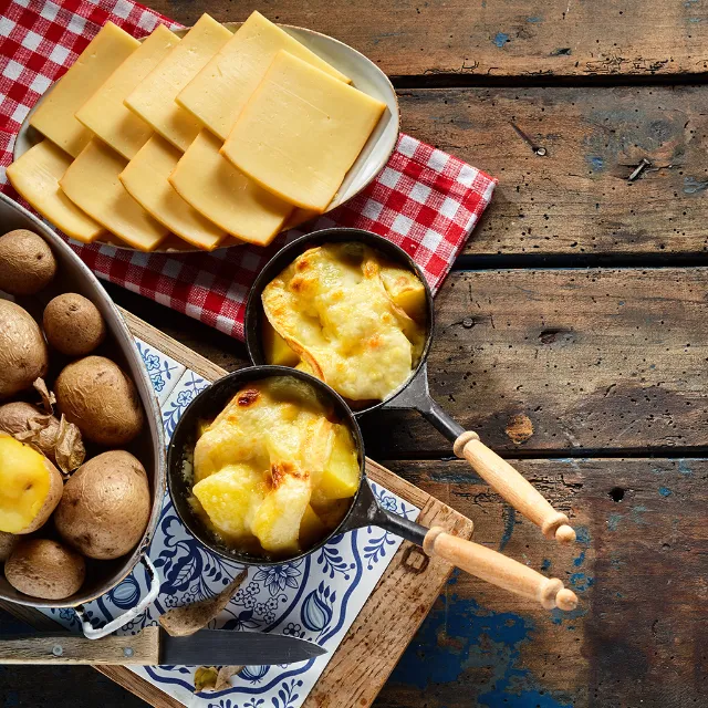 Raclettekäse über Kartoffeln im Pfännchen geschmolzen auf Holztisch