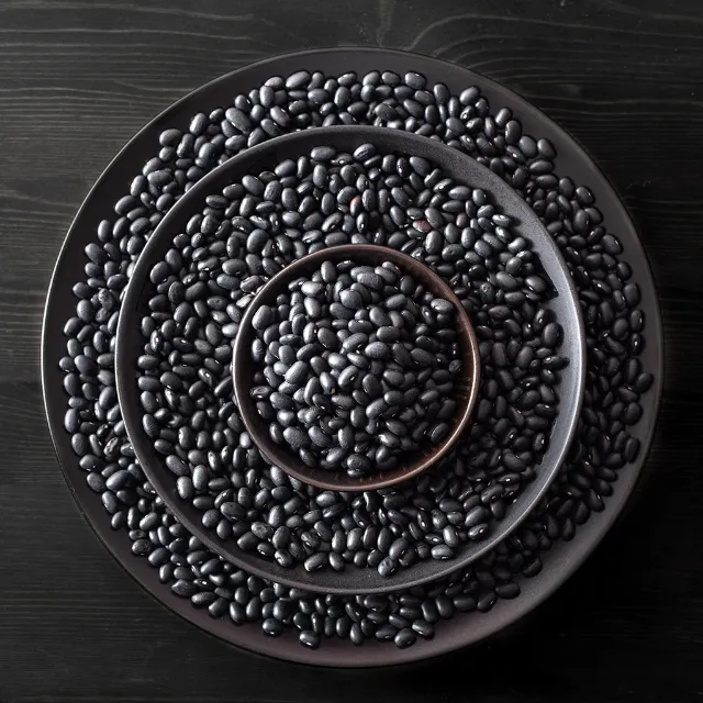 Schwarze Bohnen in drei verschiedenen schwarzen Schalen, die aufeinader stehen