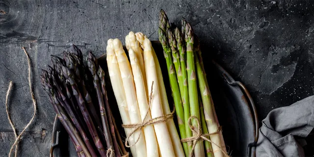 Grüner, weißer und violetter Spargel liegen auf einer Schiefernplatte