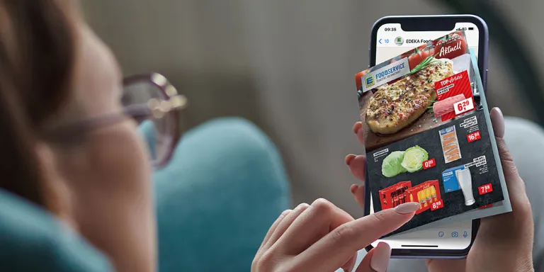 Eine Frau liegt auf dem Sofa und hat einen Blätterkatalog auf ihrem Handy geöffnet